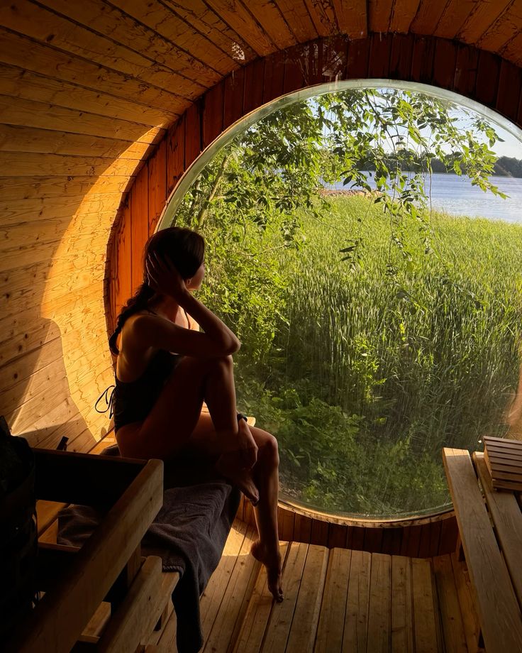 Person sitting inside a barrel sauna looking out through a round window