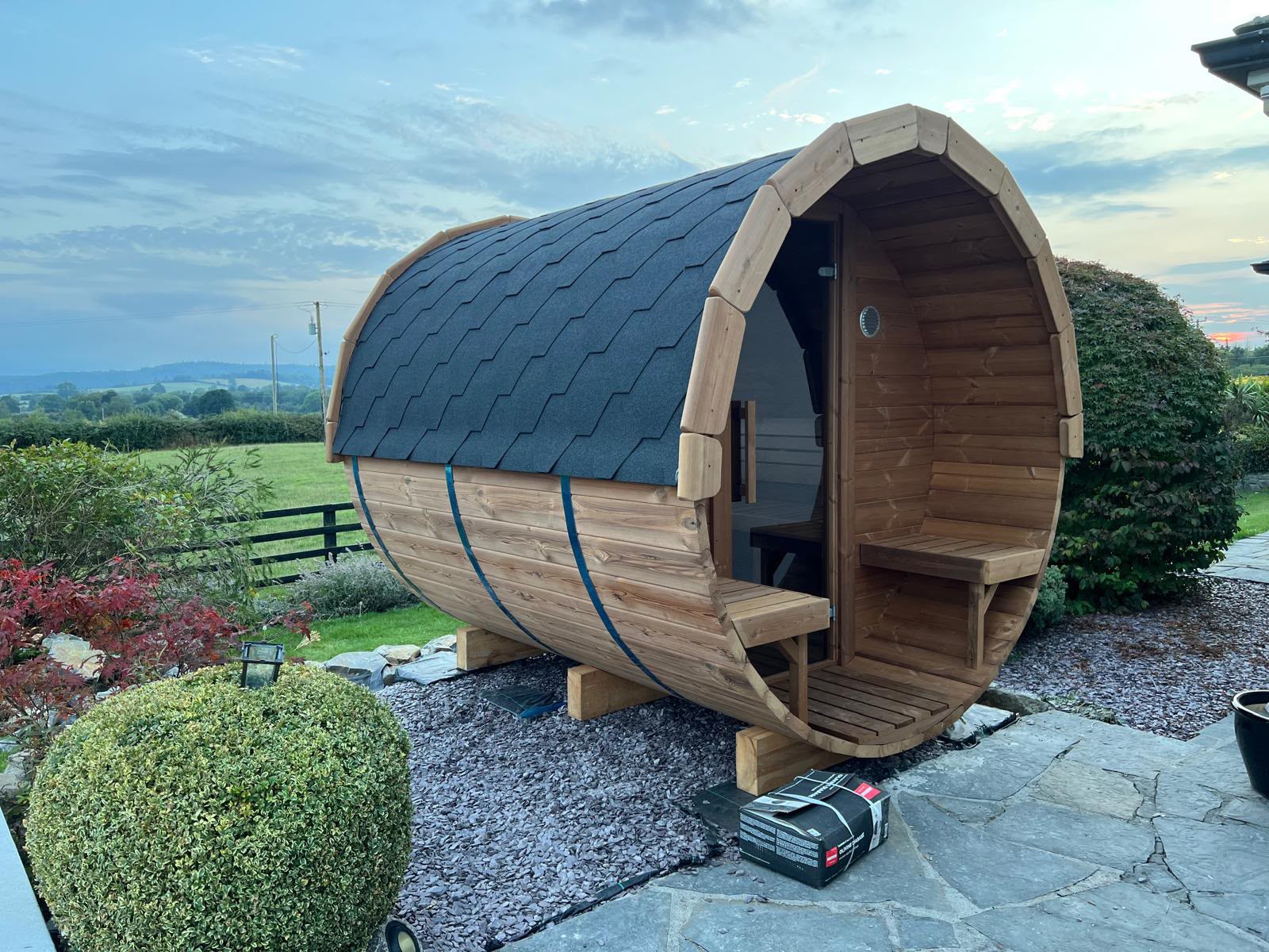 Outdoor barrel sauna with shingled roof installed in an Irish garden