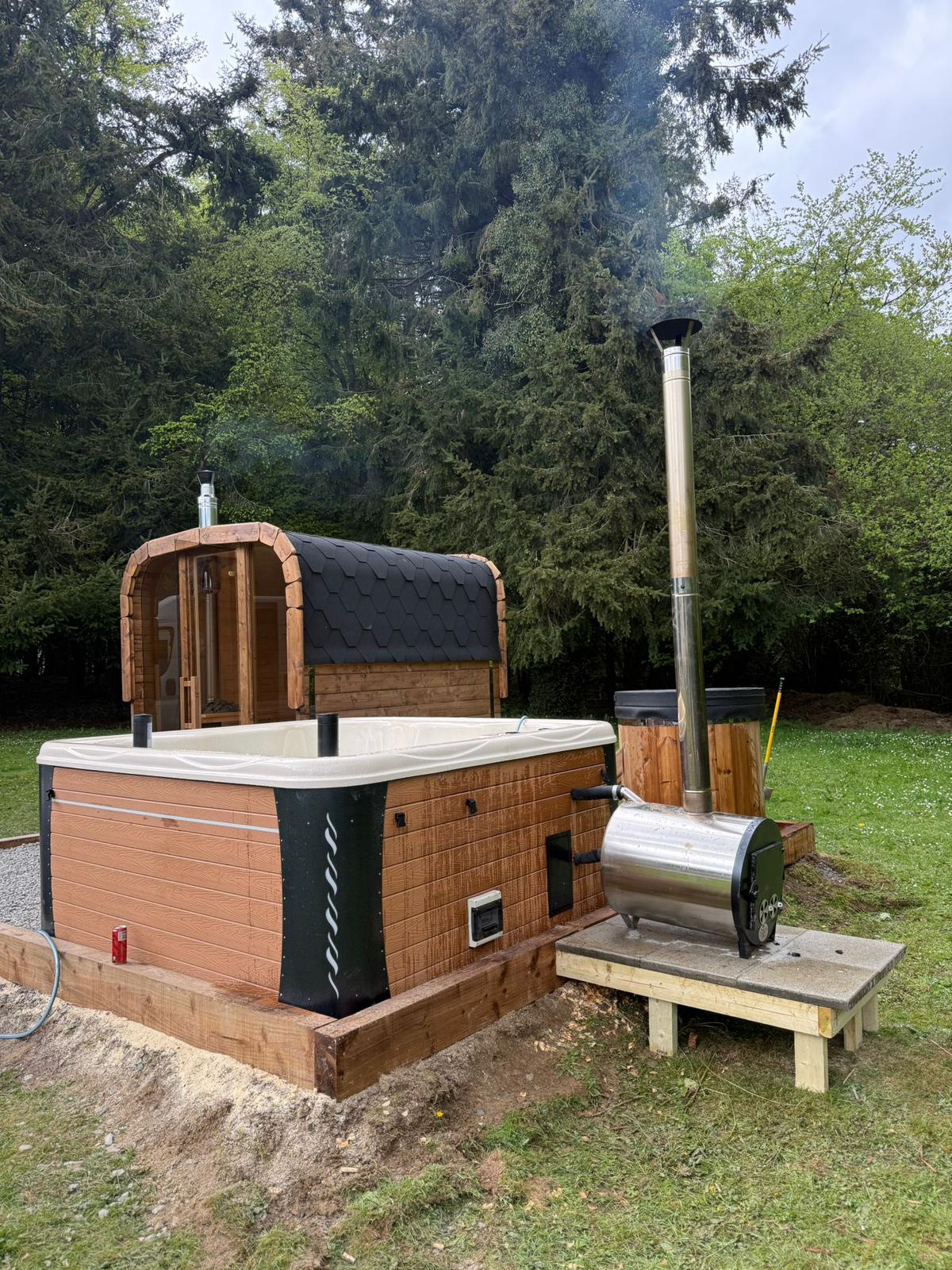 Wood-fired hot tub with external stove installed beside a barrel sauna